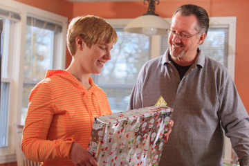 A visually impaired girl is opening a gift and her dad is standing next to her