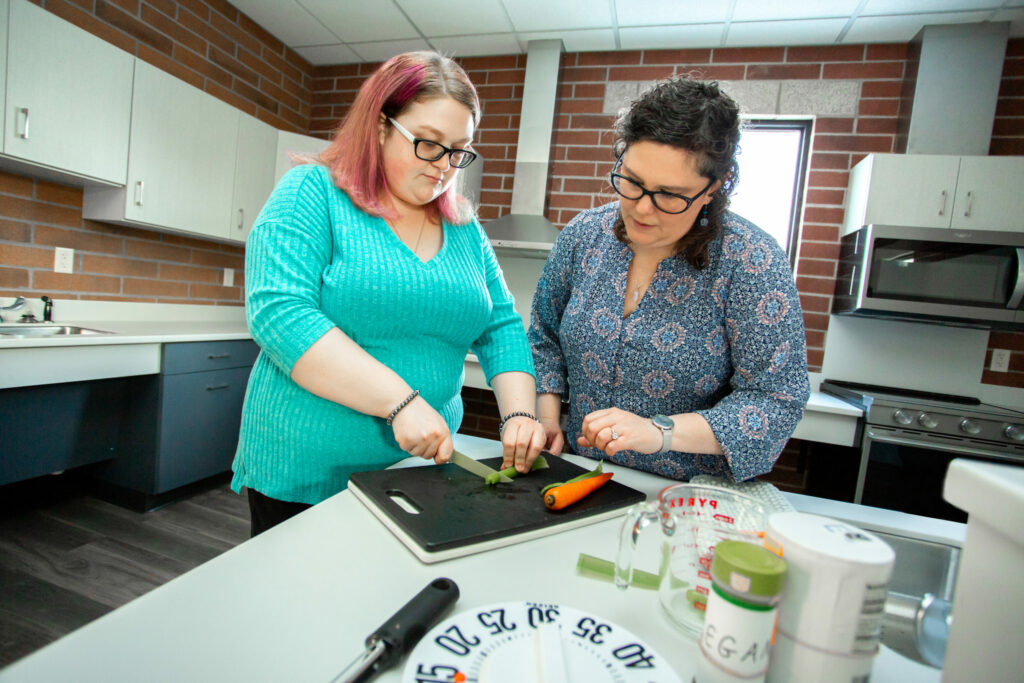 Two females in a kitchen learning vision rehabilitation therapy skills by cutting up celery