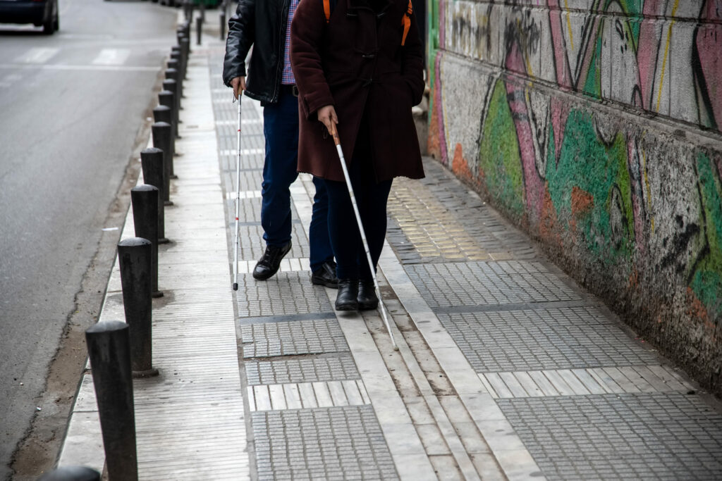 A visually impaired man and women using their white canes to track the path of tactile paving.