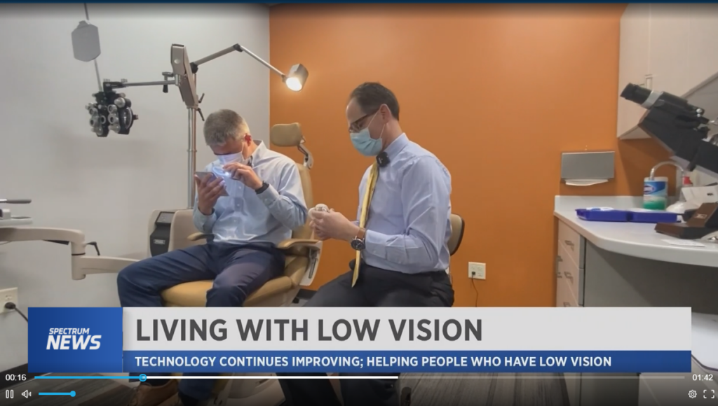 A doctor and a patient are in a low vision exam room with orange walls