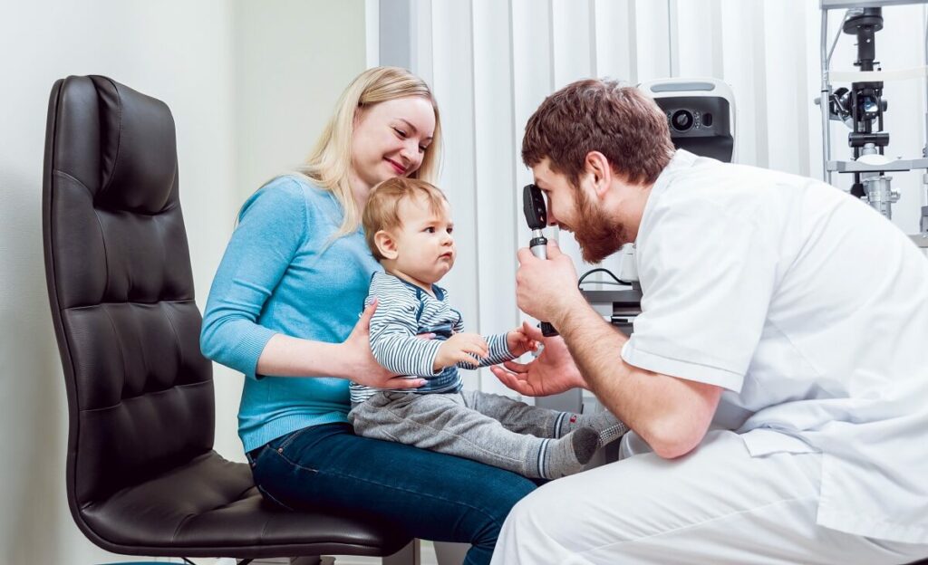 A mother holding her baby while the doctor examines the baby's eyes